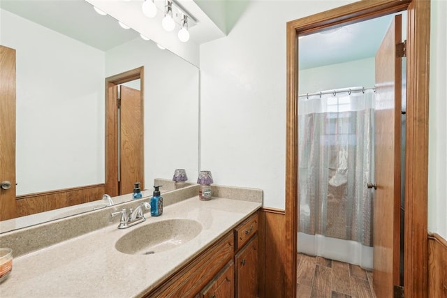full bath featuring vanity, a shower with curtain, and a wainscoted wall