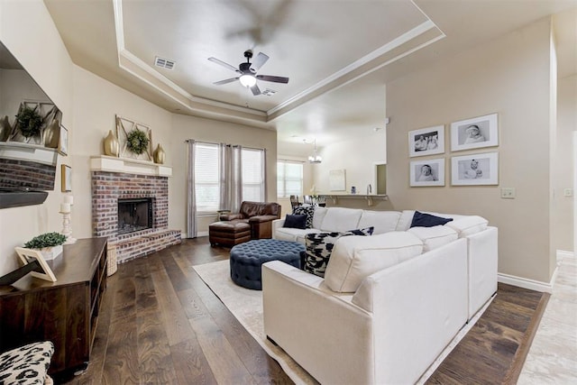 12360 Hidden Run Rd, Guthrie, OK 73044 - living room featuring a raised ceiling, ceiling fan, dark wood-type flooring, a brick fireplace, and ornamental molding