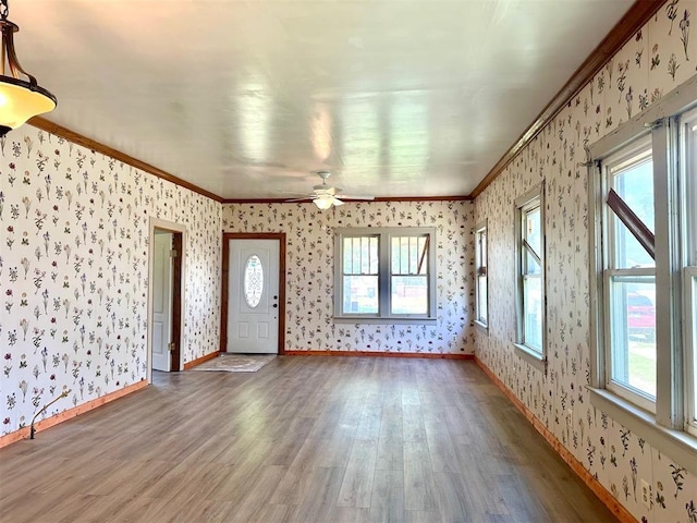 unfurnished living room featuring wallpapered walls, wood finished floors, crown molding, ceiling fan, and baseboards