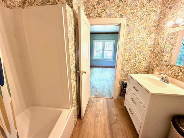 bathroom with wallpapered walls, wood finished floors, vanity, and baseboards