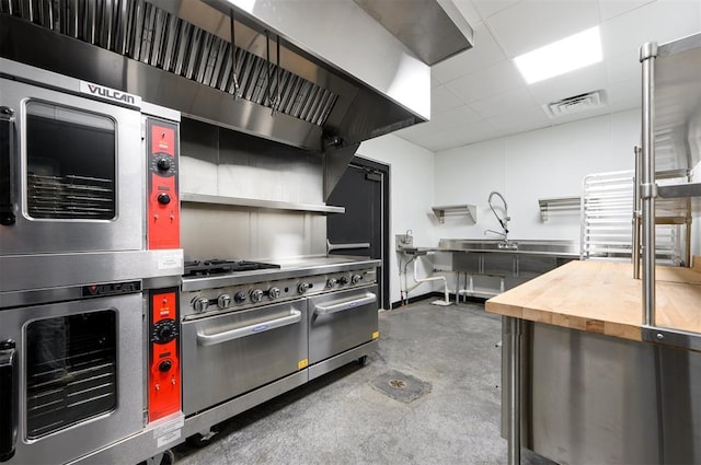 124 N Main St, Broken Bow, OK 74728 - kitchen featuring concrete flooring, stainless steel appliances, butcher block counters, a paneled ceiling, and a sink