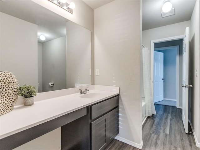 bathroom featuring wood finished floors, vanity, shower / bathtub combination with curtain, and baseboards