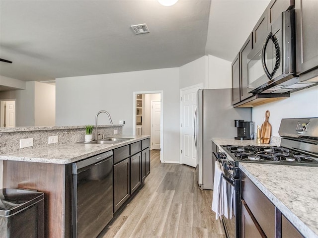 kitchen with stainless steel appliances, a sink, light wood-style floors, an island with sink, and light stone countertops