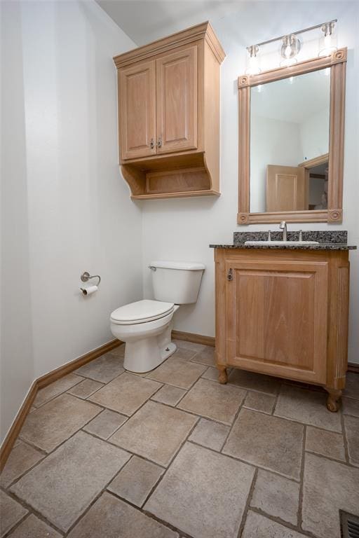 half bathroom with toilet, baseboards, vanity, and stone tile flooring