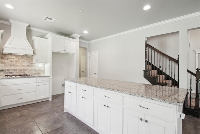5625 Courtland Ln, Choctaw, OK 73020 - kitchen with crown molding, custom range hood, tasteful backsplash, stainless steel gas cooktop, and white cabinets