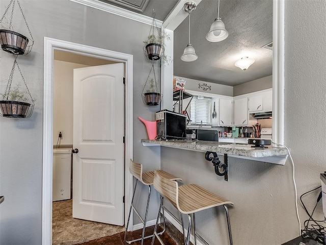 717 SW 4th Pl, Moore, OK 73160 - kitchen with under cabinet range hood, a kitchen bar, hanging light fixtures, white cabinetry, and baseboards
