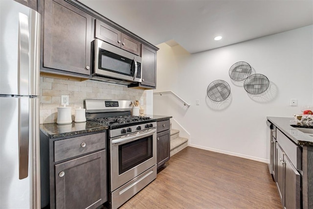 kitchen featuring appliances with stainless steel finishes, dark brown cabinetry, dark stone counters, decorative backsplash, and recessed lighting