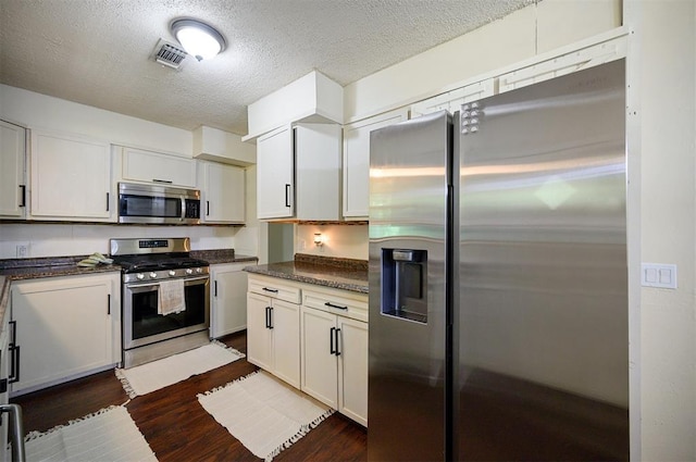 308 E Highland St, Hugo, OK 74743 - kitchen featuring appliances with stainless steel finishes, dark countertops, dark wood-style flooring, and a textured ceiling