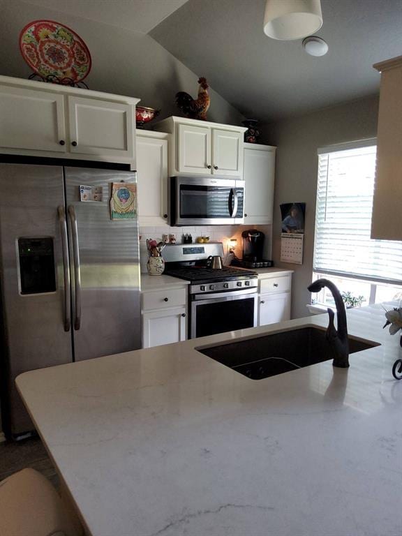 kitchen with appliances with stainless steel finishes, a sink, white cabinets, backsplash, and lofted ceiling
