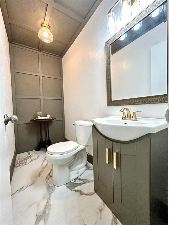 4008 Creekwood, Edmond, OK 73025 - half bath with marble finish flooring, toilet, vanity, and a decorative wall