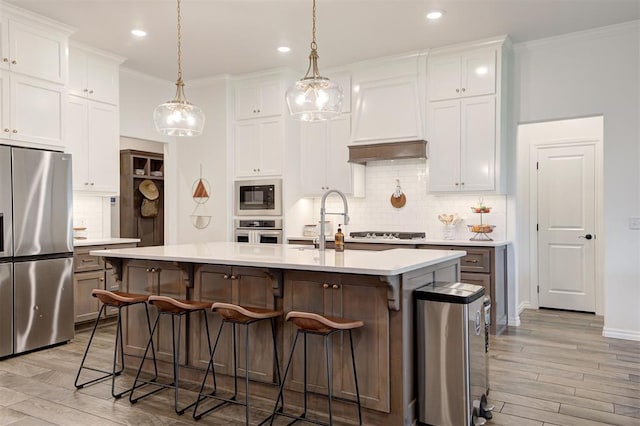 kitchen with stainless steel appliances, tasteful backsplash, light countertops, a breakfast bar area, and a center island with sink