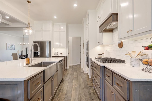 kitchen with appliances with stainless steel finishes, white cabinetry, decorative backsplash, ornamental molding, and wood finished floors