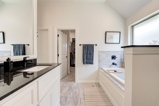 bathroom with vaulted ceiling, a bath, a spacious closet, and vanity