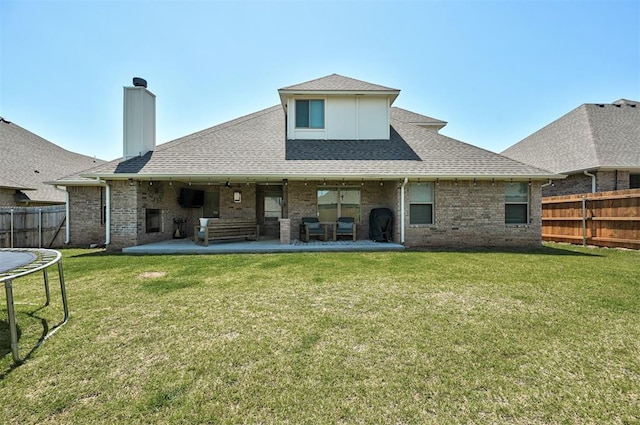 rear view of house featuring a trampoline, brick siding, roof with shingles, and a patio area