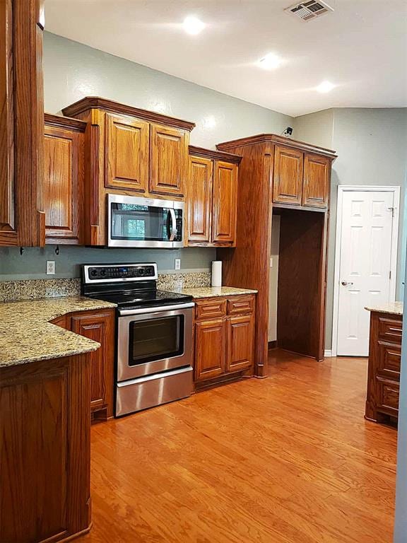 7336 E 136th Rd, Holdenville, OK 74848 - kitchen featuring appliances with stainless steel finishes, light wood-type flooring, brown cabinets, and light stone counters