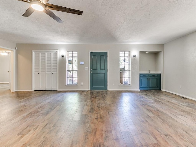1400 Brookhaven Dr, Edmond, OK 73034 - unfurnished living room featuring a textured ceiling, ceiling fan, wood-type flooring, and baseboards