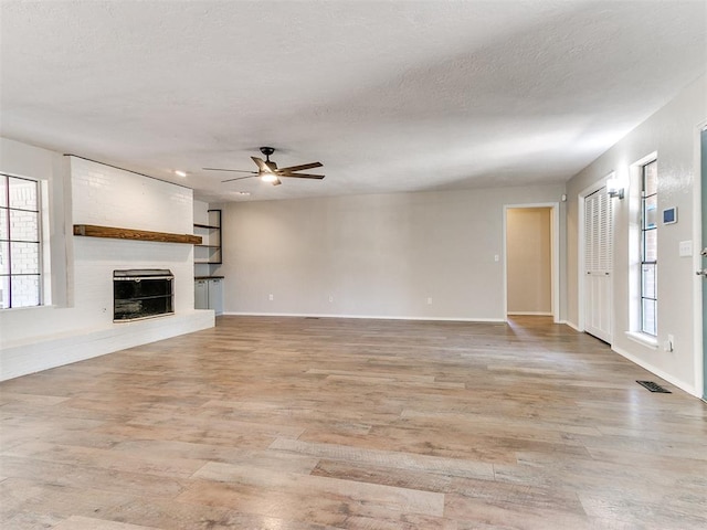 1400 Brookhaven Dr, Edmond, OK 73034 - unfurnished living room featuring ceiling fan, light wood-style flooring, plenty of natural light, a fireplace, and a textured ceiling