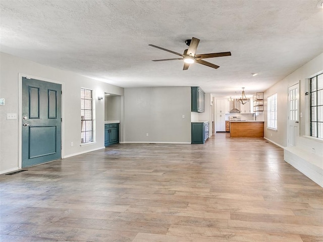 1400 Brookhaven Dr, Edmond, OK 73034 - unfurnished living room featuring light wood-style floors, a ceiling fan, a textured ceiling, a chandelier, and baseboards