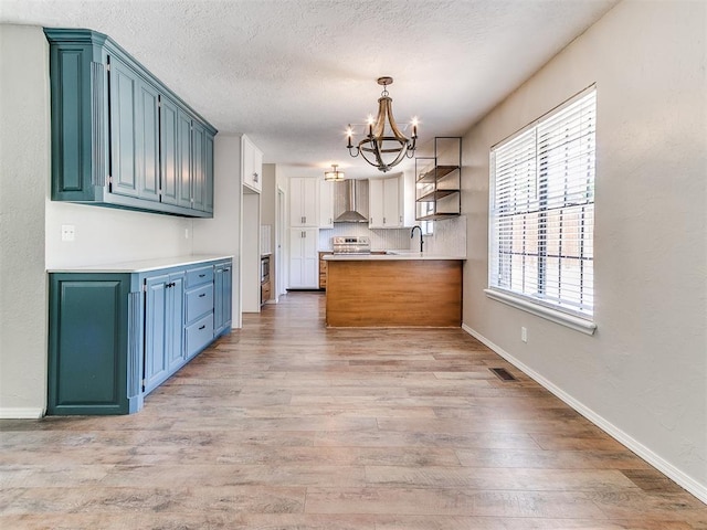 1400 Brookhaven Dr, Edmond, OK 73034 - kitchen featuring a chandelier, light wood-type flooring, wall chimney exhaust hood, a peninsula, and baseboards