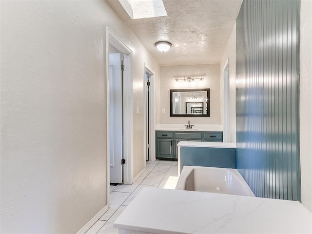 1400 Brookhaven Dr, Edmond, OK 73034 - bathroom with baseboards, a tub, a skylight, vanity, and a textured wall