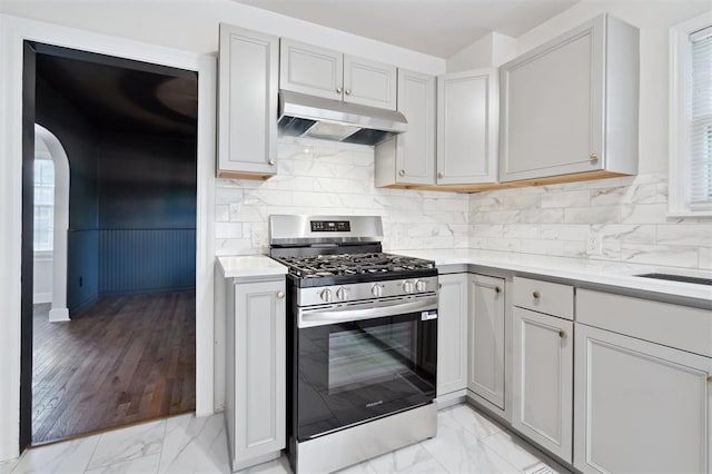 2321 NW 25th St, Oklahoma City, OK 73107 - kitchen with gas stove, under cabinet range hood, light countertops, light marble finish flooring, and a wainscoted wall