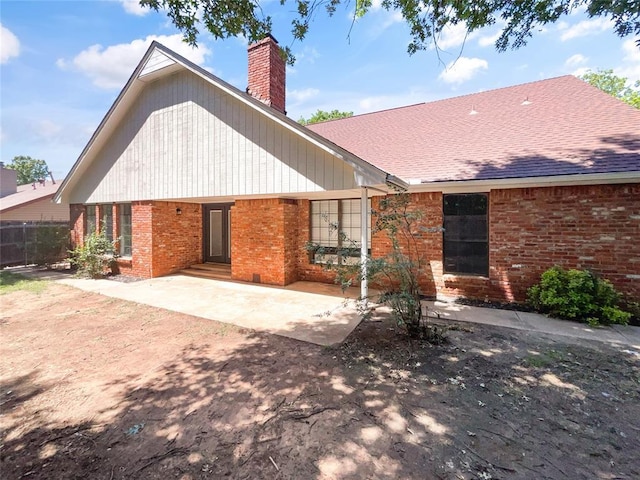 view of front of house with brick siding, a chimney, a patio, fence, and a shingled roof