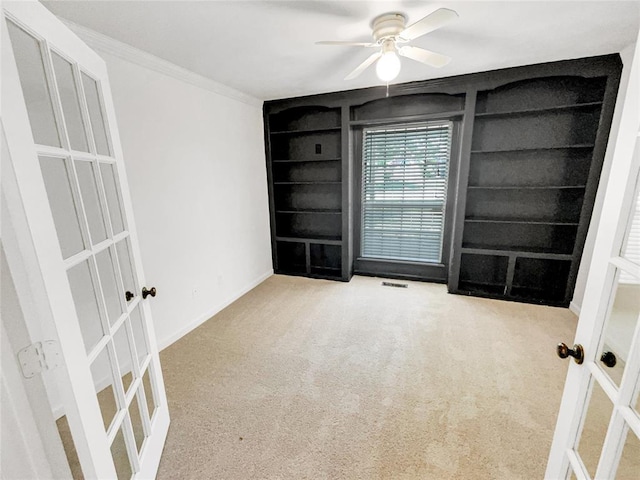 carpeted empty room with built in features, ceiling fan, crown molding, french doors, and baseboards