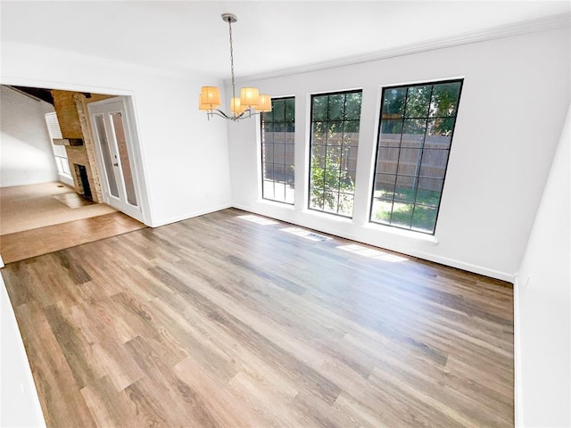 unfurnished dining area with a chandelier, wood finished floors, a brick fireplace, baseboards, and ornamental molding