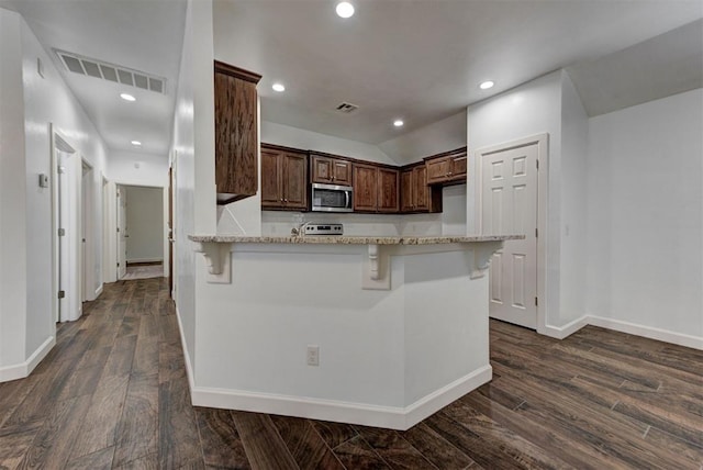 316 SW 4th Pl, Newcastle, OK 73065 - kitchen with stainless steel microwave, a breakfast bar area, a peninsula, dark wood-style floors, and recessed lighting