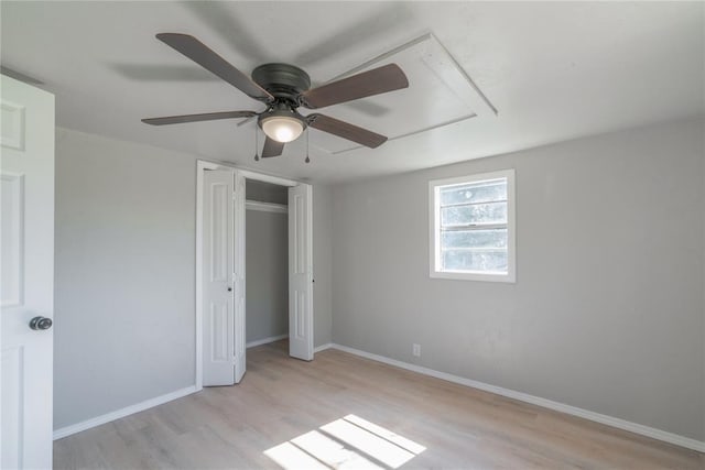 unfurnished bedroom with attic access, light wood-type flooring, baseboards, ceiling fan, and a closet