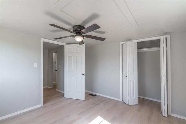 unfurnished bedroom with attic access, light wood-style floors, baseboards, a closet, and a ceiling fan