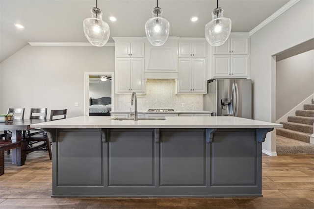 kitchen featuring stainless steel refrigerator with ice dispenser, a sink, crown molding, light countertops, and an island with sink