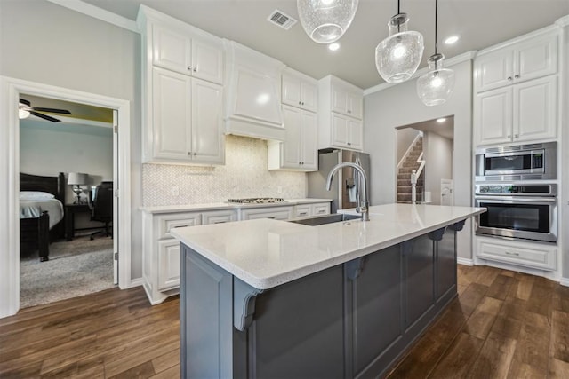 kitchen with appliances with stainless steel finishes, a sink, dark wood-type flooring, white cabinetry, and tasteful backsplash