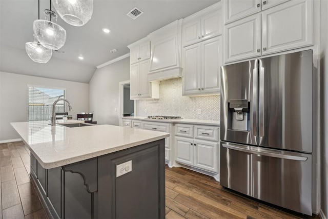 kitchen featuring stainless steel appliances, a sink, backsplash, a center island with sink, and white cabinets