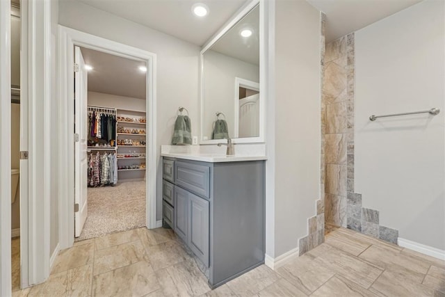 full bath with vanity, a walk in closet, recessed lighting, a tile shower, and baseboards