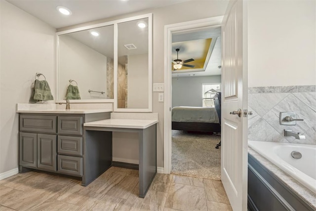 ensuite bathroom featuring ceiling fan, vanity, a tub to relax in, baseboards, and recessed lighting