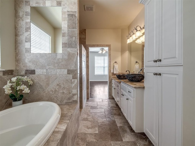 16104 Ledge Ln, Edmond, OK 73013 - bathroom with stone tile floors, tiled bath, vanity, and a ceiling fan