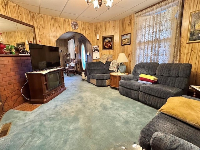 living room featuring arched walkways, wooden walls, carpet floors, and a paneled ceiling