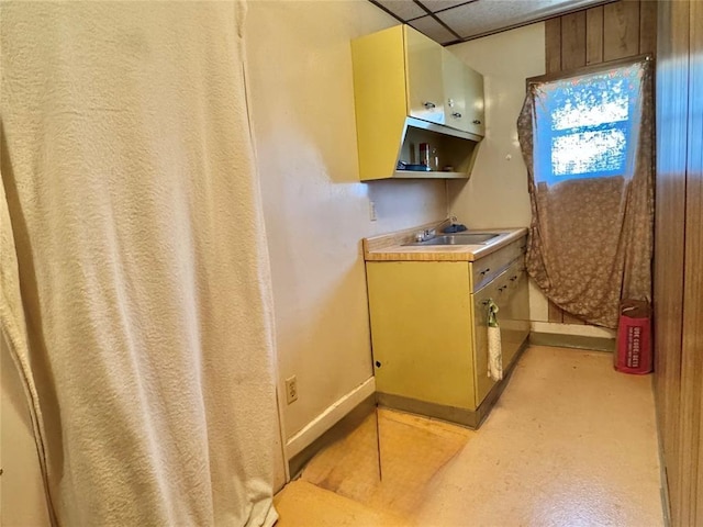kitchen with a sink, baseboards, a drop ceiling, light countertops, and open shelves