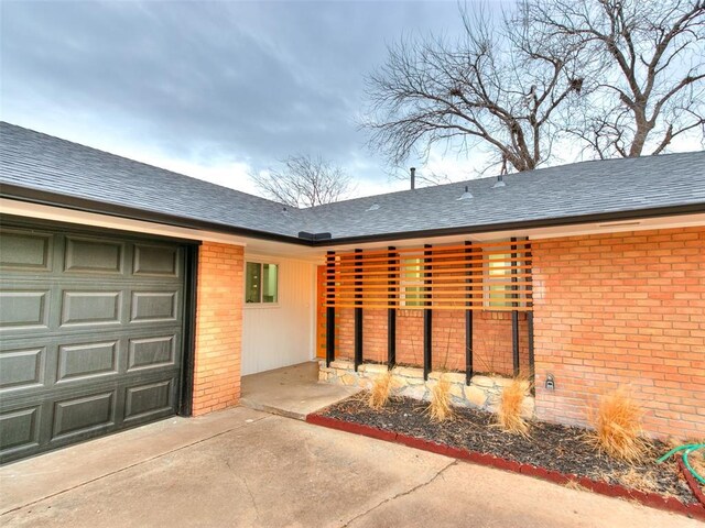 3325 NW 65th St, Oklahoma City, OK 73116 - doorway to property featuring brick siding, a garage, driveway, and a shingled roof