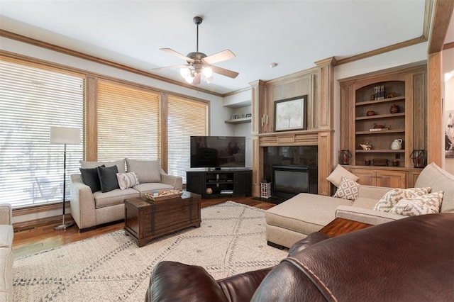 living room featuring a fireplace, wood finished floors, ceiling fan, crown molding, and built in shelves