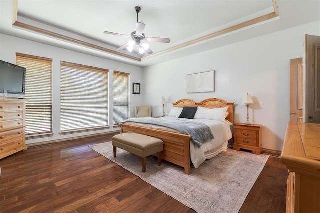 bedroom with a tray ceiling, dark wood-type flooring, crown molding, a ceiling fan, and baseboards