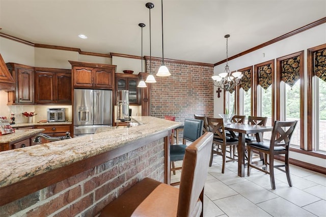 kitchen with stainless steel refrigerator with ice dispenser, ornamental molding, light tile patterned floors, light stone counters, and a chandelier