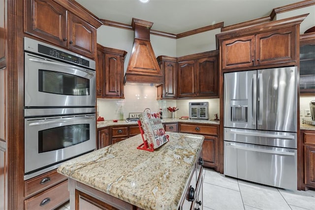 kitchen with stainless steel appliances, custom range hood, tasteful backsplash, light tile patterned floors, and light stone counters