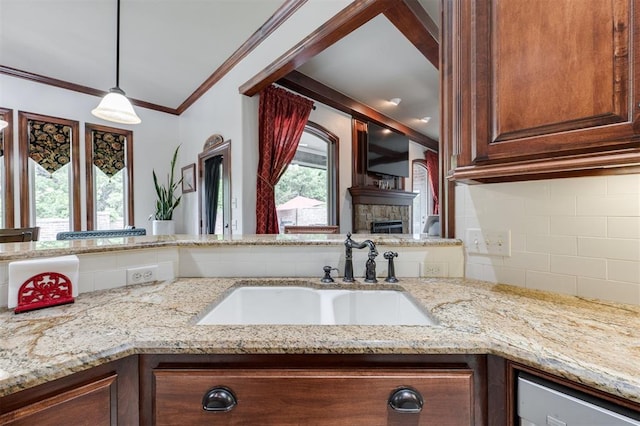 kitchen with a sink, crown molding, light stone countertops, decorative backsplash, and hanging light fixtures