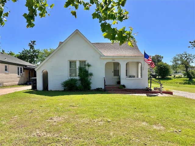 english style home with stucco siding, a front lawn, a porch, and a shingled roof