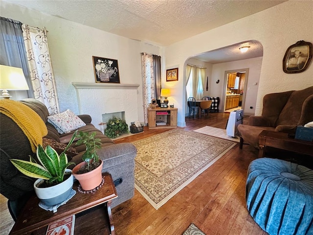 living area featuring arched walkways, hardwood / wood-style floors, a textured ceiling, and a textured wall