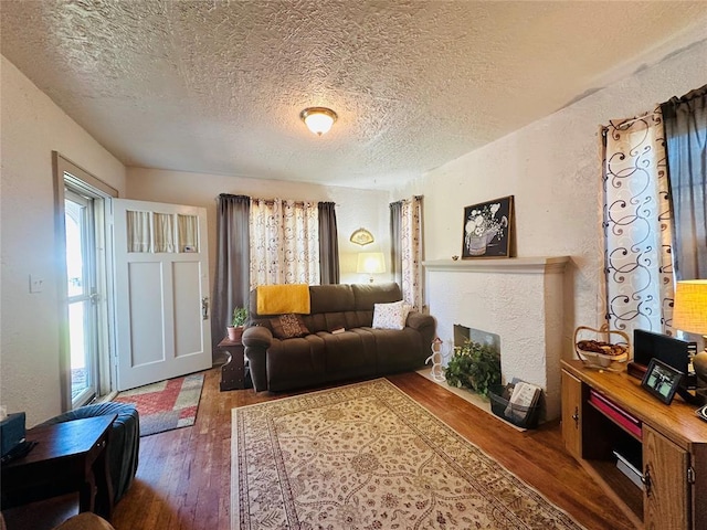 living area featuring a textured ceiling, a textured wall, wood-type flooring, and a fireplace with flush hearth