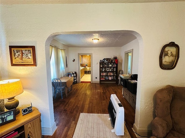 hall with arched walkways, heating unit, a textured wall, wood finished floors, and baseboards