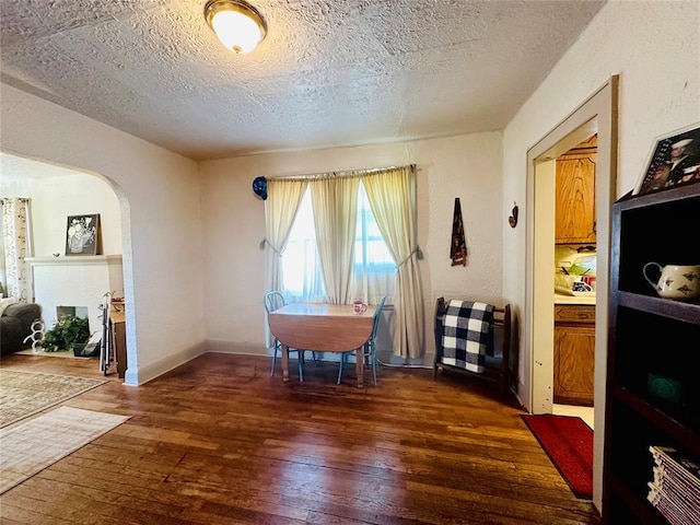 dining room with wood-type flooring, a textured ceiling, arched walkways, and baseboards